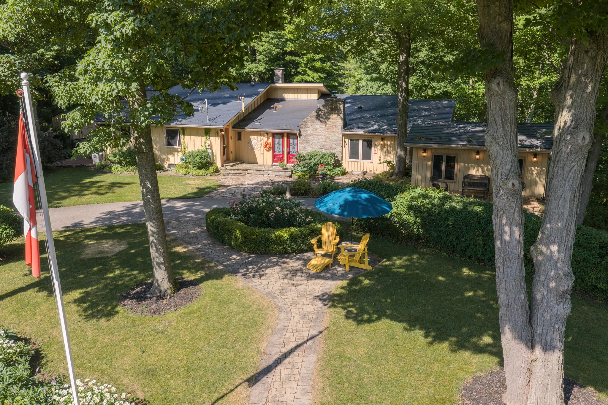 Aerial drone photograph of a Heritage Road estate home with its lawn, flagpole and garden seating among the trees. RCG Canada real estate photography